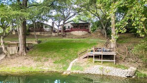 Una propiedad frente al lago con muelle de piedra, terraza de madera y una casa con barandal rojo y porche.