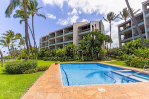 A swimming pool surrounded by palm trees and a building with multiple balconies.