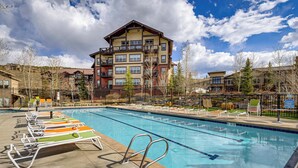 A swimming pool with lounge chairs, a multi-story building in the background, and a clear sky. - Granby Home w/ Hot Tub + Ski, Golf & Pool Access (Granby)