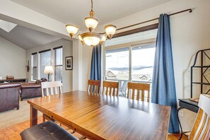 A dining area with a wooden table, chairs, a chandelier, and a view through large windows. - Granby Home w/ Hot Tub + Ski, Golf & Pool Access (Granby)