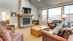 A living room with a fireplace, leather sofas, a coffee table, and large windows with a view. - Granby Home w/ Hot Tub + Ski, Golf & Pool Access (Granby)