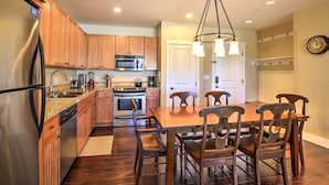 A kitchen with wooden cabinets, a stainless steel refrigerator, a microwave, and a dining table with chairs. - Ski-In/Ski-Out Access: Mtn-View Granby Condo! (Granby)