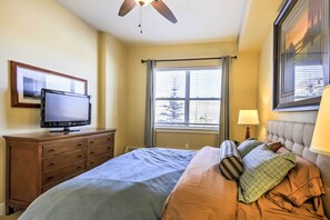 Ein Schlafzimmer mit einem Bett, einem Fernseher auf einer Kommode, einem Fenster mit Vorhängen und einem Deckenventilator.