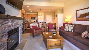 A living room with a fireplace, a sofa, a coffee table, and a TV mounted on the wall. - Ski-In/Ski-Out Access: Mtn-View Granby Condo! (Granby)