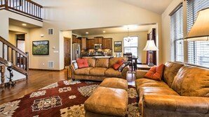 A spacious living room with a leather sofa, ottoman, and a patterned rug. A staircase leads to an upper level. - Patio, Fire Pit, & Ski Mountain View: Granby Home (Granby)