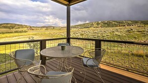 A covered outdoor area with a table and chairs, overlooking a rural landscape with houses and fields. - Patio, Fire Pit, & Ski Mountain View: Granby Home (Granby)