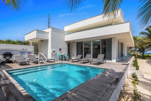 Et moderne poolområde med en klar, blå pool, liggestole og en grill.