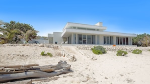 Una moderna casa sulla spiaggia con tetto piatto, ampie finestre e un muro di sostegno in pietra.