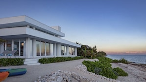 Una moderna proprietà fronte mare con ampia facciata vetrata, area relax esterna coperta e vista sul mare.