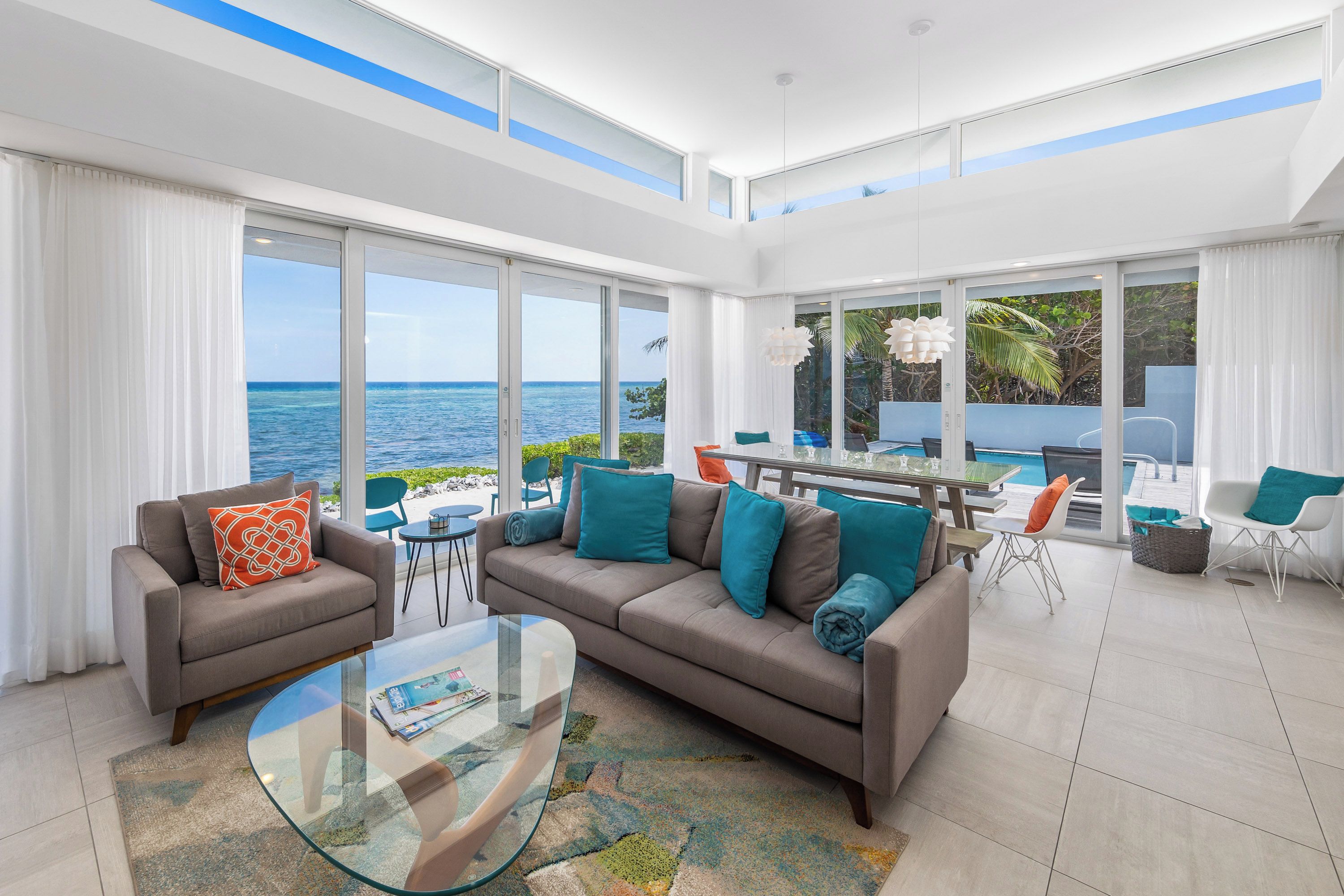 A spacious living area with a large sofa, a glass coffee table, and a view of the ocean.