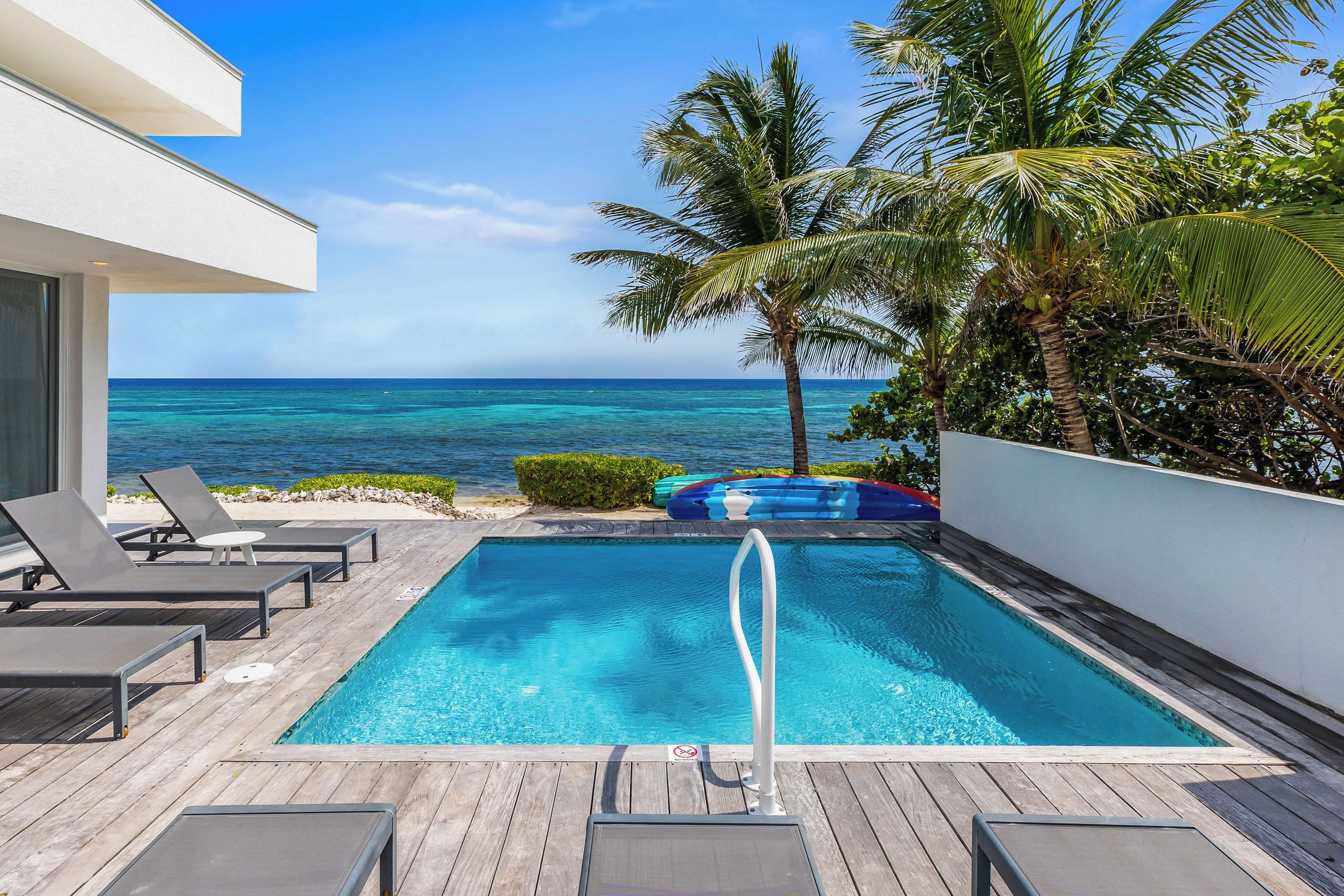 A pool with a view of the ocean, surrounded by lounge chairs and palm trees.