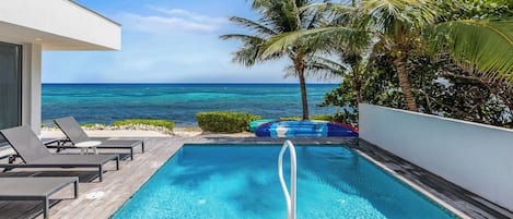 A pool with a view of the ocean, surrounded by lounge chairs and palm trees.