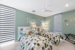 Ein Schlafzimmer mit zwei Betten, einem Deckenventilator, Wanddekorationen mit Sternenmotiven und einem Fenster mit Jalousien.