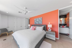 Une chambre à coucher comprenant un lit, des tables de chevet, une chaise, un ventilateur de plafond et une armoire.