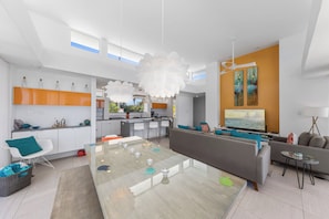 A modern living room with a glass coffee table, a sofa, and a dining area with chairs. - Villa Esprit–Stunning beachfront villa in North Side w/pool-by Cayman Villas (North Side)