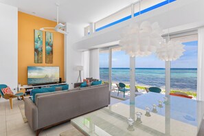 A modern living room with a large sofa, a flat-screen TV, and artwork on the wall. - Villa Esprit–Stunning beachfront villa in North Side w/pool-by Cayman Villas (North Side)