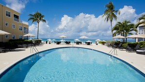 Ein Swimmingpool mit Liegestühlen und Sonnenschirmen, umgeben von Palmen und einem Gebäude mit Balkonen.