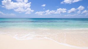 A beach with clear turquoise water and white sand. - Laguna Del Mar 24 -  3rd floor luxury condo on 7MB - Call Cayman Villas! (Seven Mile Beach)