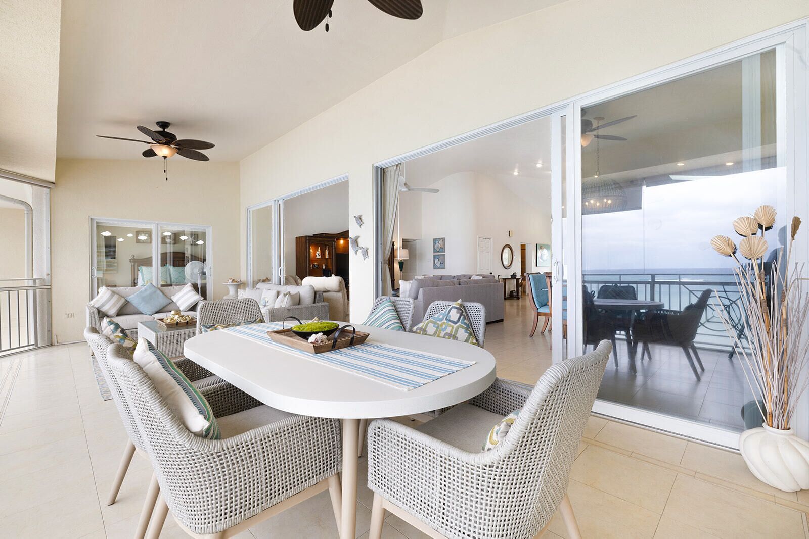 A spacious living area with a round dining table, wicker chairs, and a balcony with a view.
