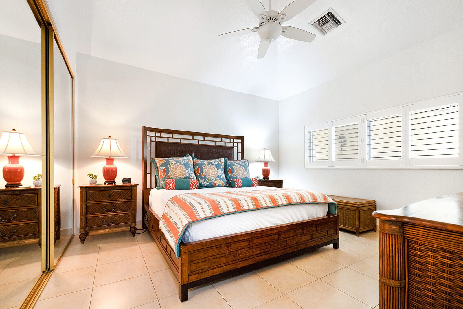 A bedroom with a wooden bed, two bedside tables with lamps, a ceiling fan, and a window with blinds.