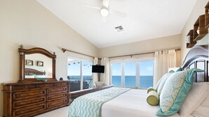 A bedroom with a large bed, a dresser, a ceiling fan, a TV, and a balcony with a view of the ocean. - Laguna Del Mar 24 -  3rd floor luxury condo on 7MB - Call Cayman Villas! (Seven Mile Beach)