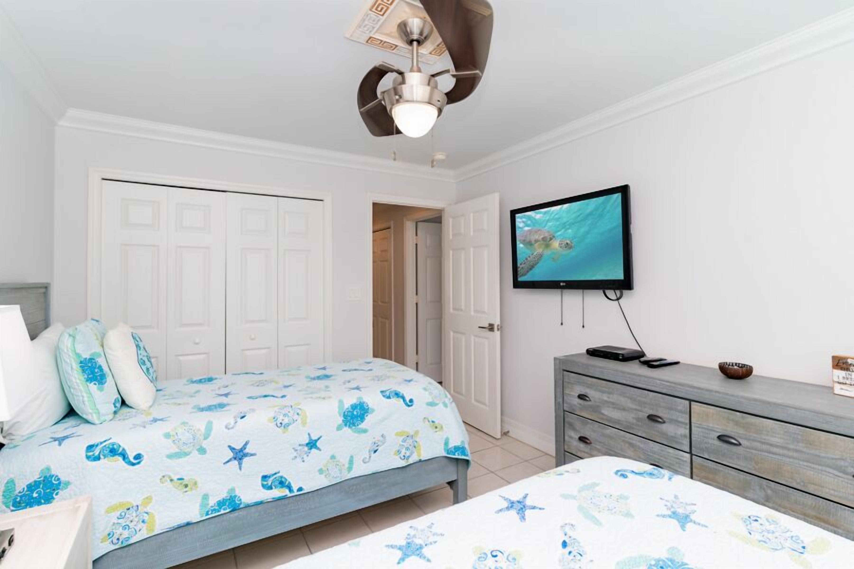 Een slaapkamer met een bed, een dressoir, een televisie en een plafondventilator.