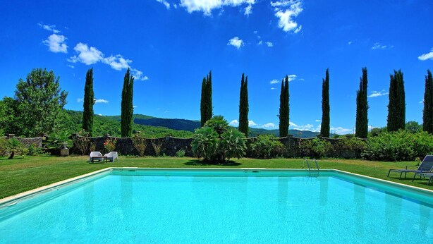 A rectangular swimming pool with clear blue water, surrounded by a well-maintained lawn and tall cypress trees. - Villa Capolona - Villa Rental with swimming pool in Casentino Valley, Tuscany (Subbiano)