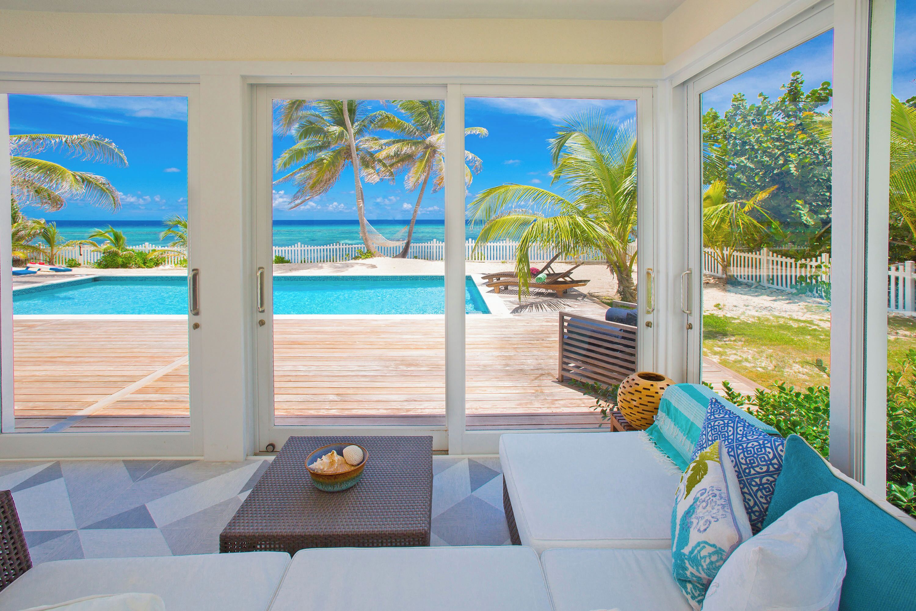 Ein Zimmer mit einer großen Schiebetür, die zu einem Poolbereich mit Holzterrasse und Palmen führt.