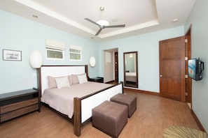 A bedroom with a bed, bedside tables, a ceiling fan, a large mirror, and a television.