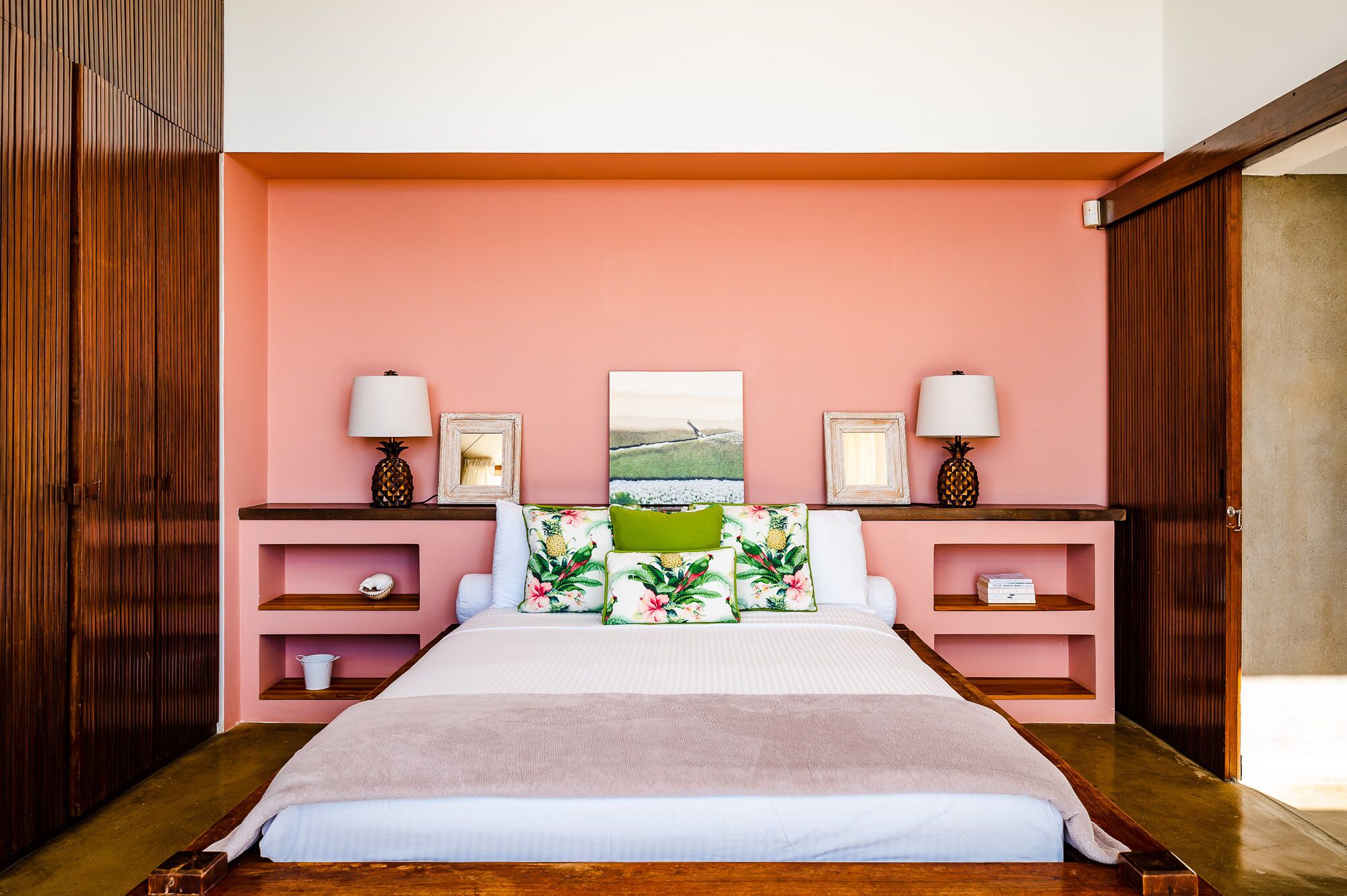 A bedroom with a bed, two nightstands, a wooden wardrobe, and a pink wall.