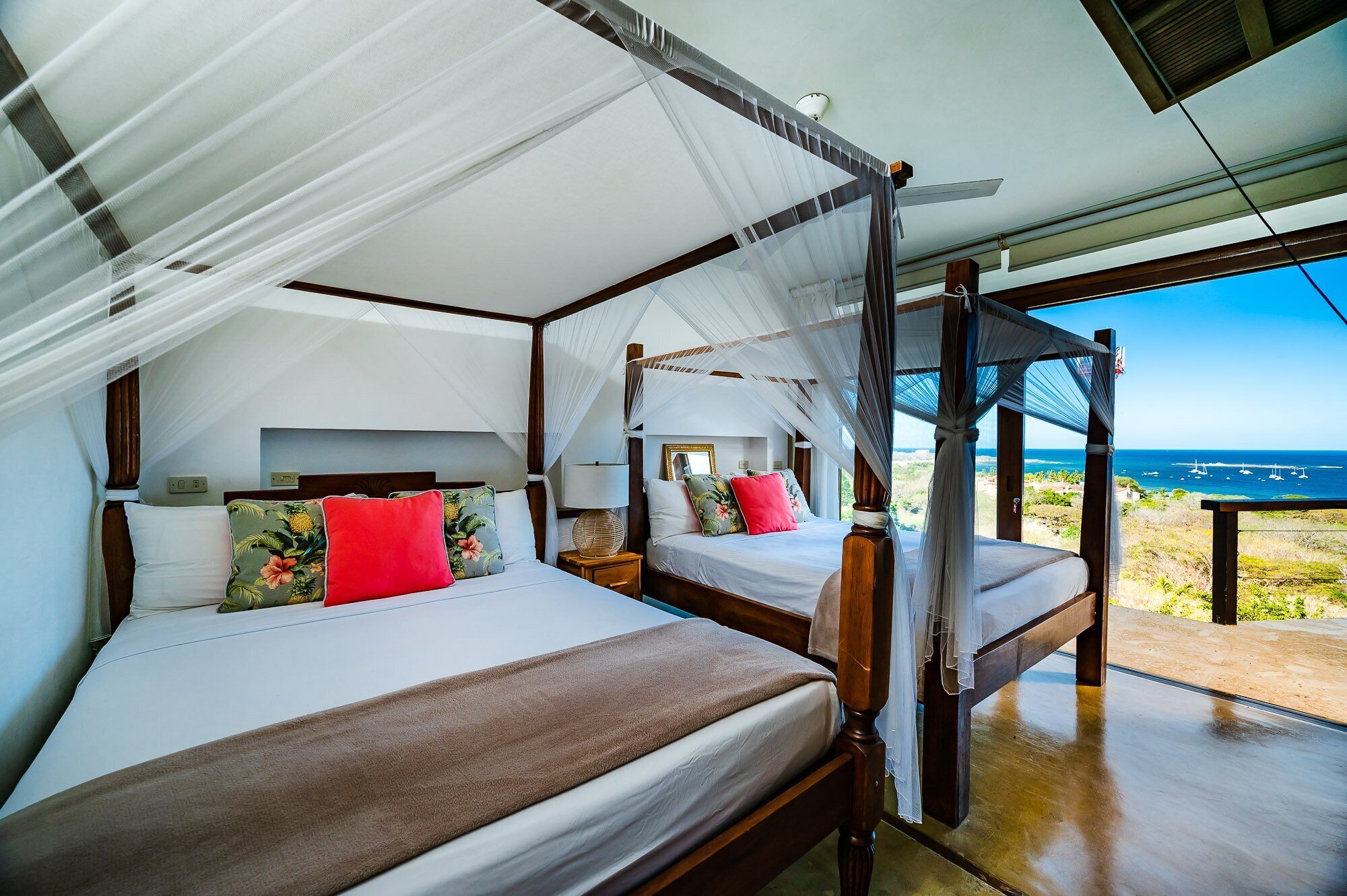 Un dormitorio con dos camas, cada una con dosel, y un ventanal con vistas al océano.