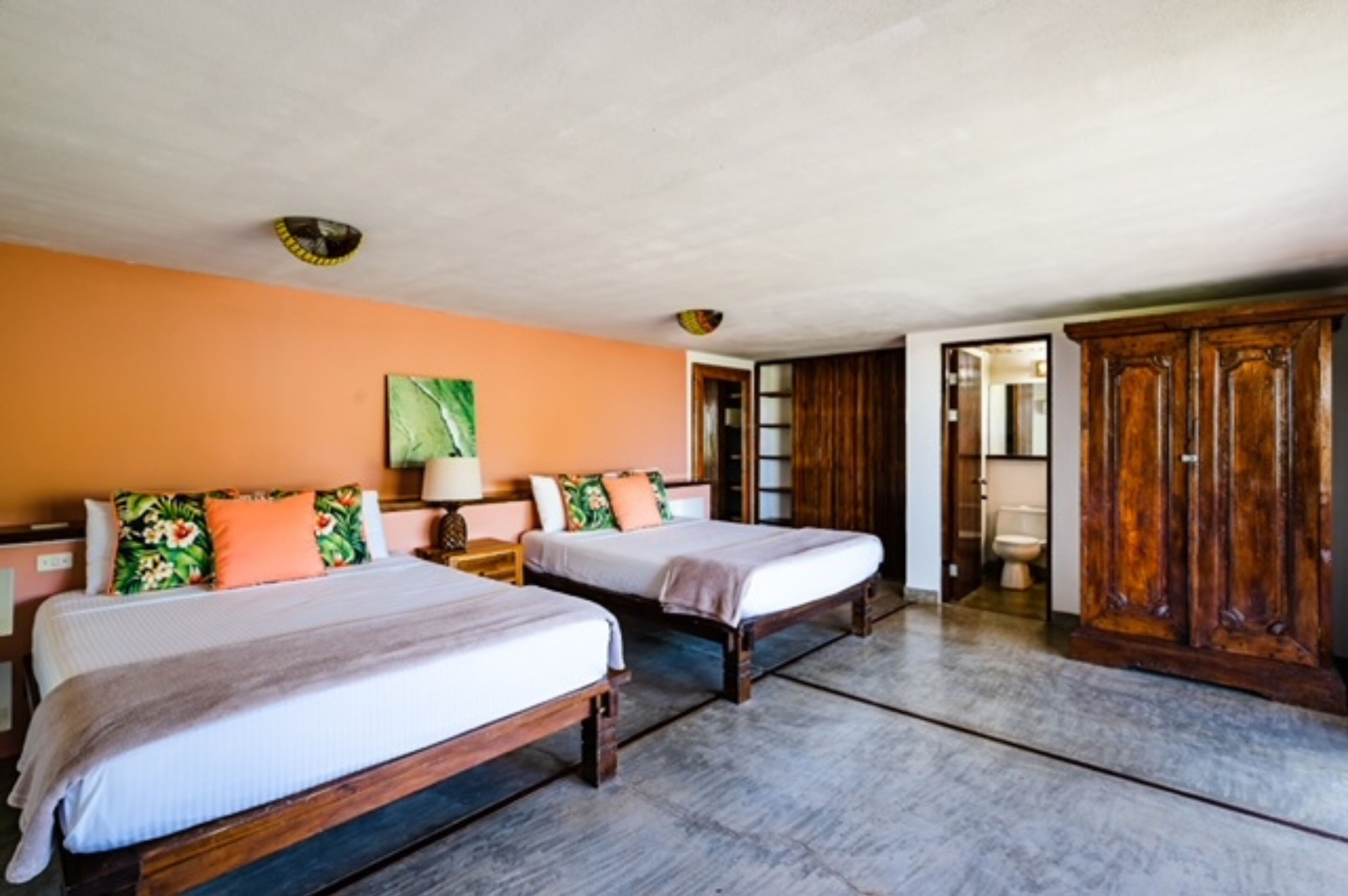 A hotel room with two beds, a wooden wardrobe, and a bathroom visible through an open door.