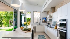 A modern kitchen with white cabinetry, stainless steel appliances, and a large island with fruit and flowers. - Ocean Views · Infinity Pool · 3 min to the Beach & Exclusive Beach Club Access (Tamarindo)