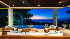 A modern outdoor seating area with wooden furniture and a view of the ocean at dusk. - Ocean Views · Infinity Pool · 3 min to the Beach & Exclusive Beach Club Access (Tamarindo)