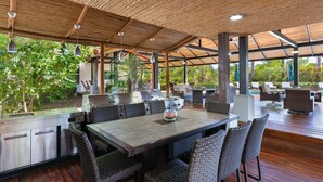 Un patio al aire libre con una mesa de madera y sillas de mimbre, rodeado por una estructura cubierta con techo de bambú.