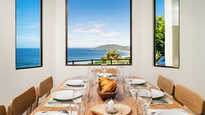 A dining table set for six with a view of the ocean through large windows.