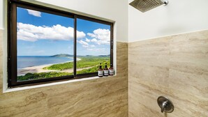 A bathroom with a large window offering a view of a beach and ocean.