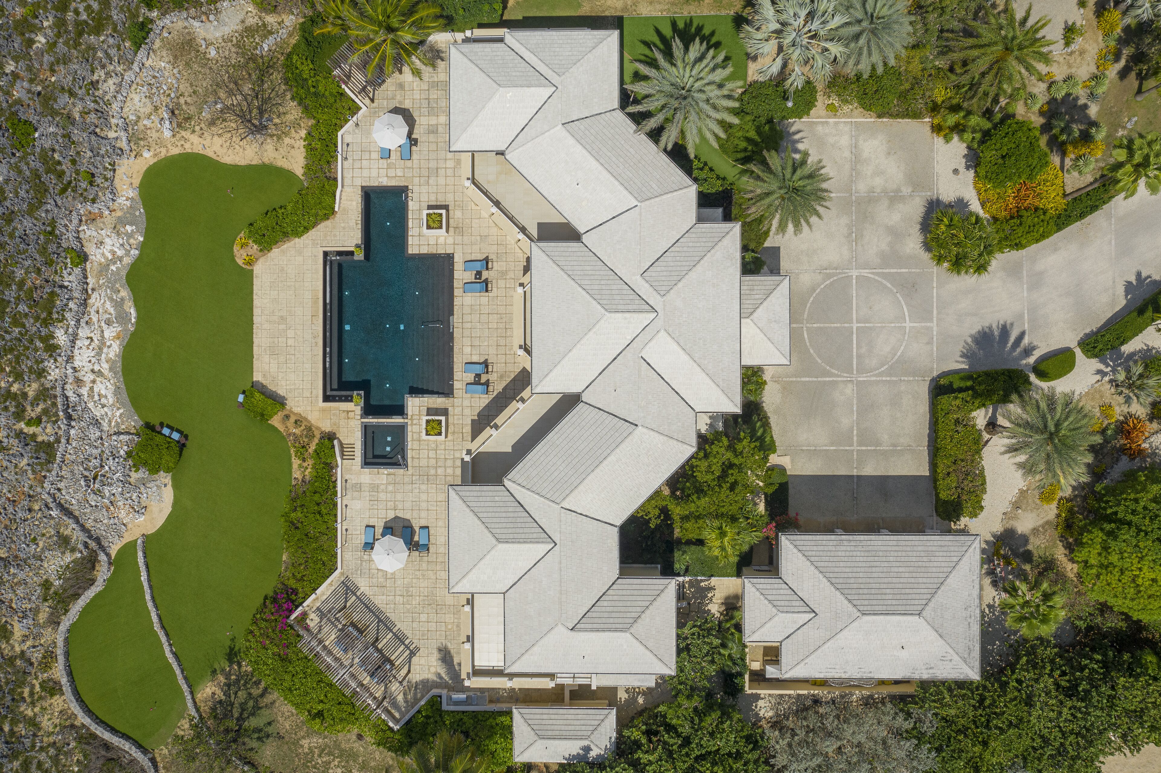 Una vista aerea di una casa moderna con piscina, campo da tennis e giardino curato.