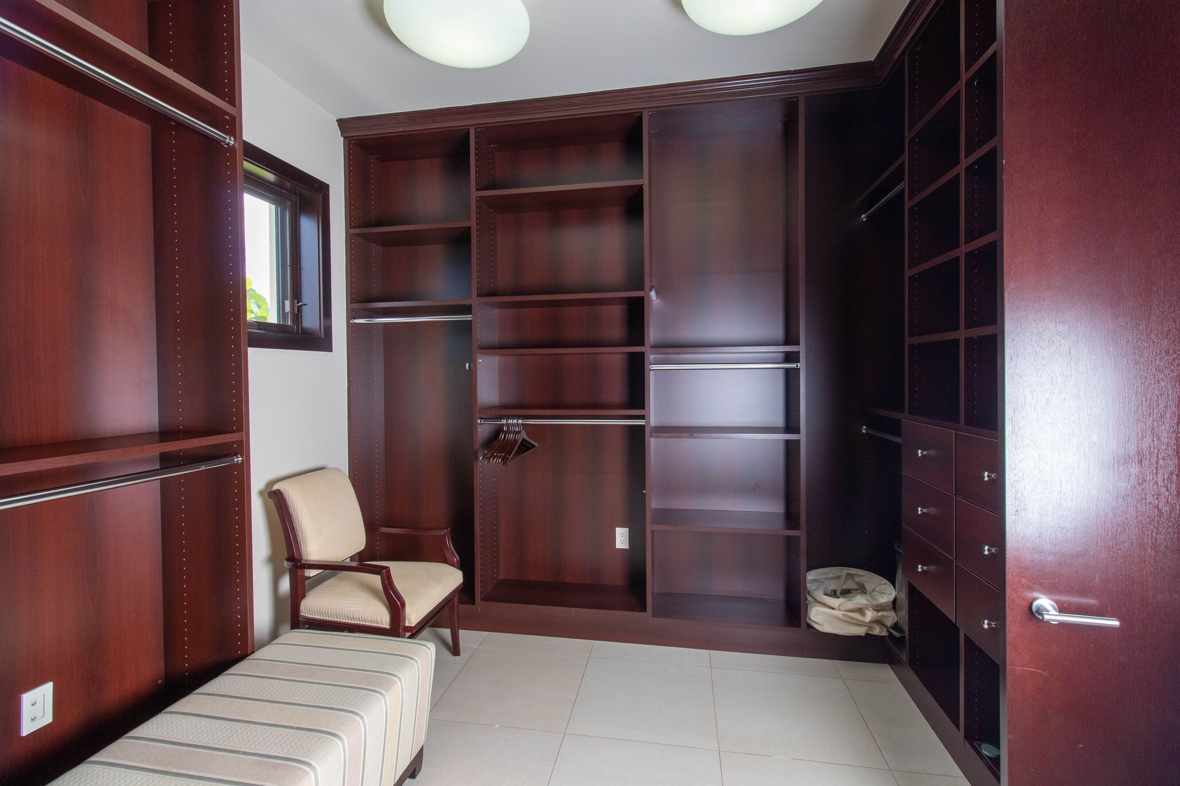 Un vestidor amplio con varios estantes y cajones, una silla y una maleta.