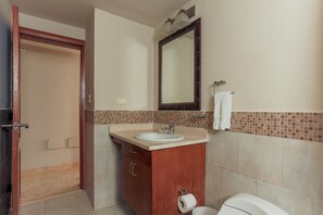 A bathroom with a wooden vanity, a sink, a mirror, and a toilet. - Playa Turquesa K301_200Mbps_Private Beach Access_BBQ_Pools (Punta Cana)
