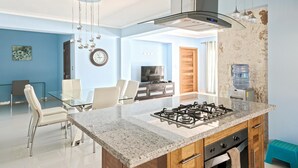 Une cuisine moderne équipée d’une cuisinière à gaz, de meubles en bois et d’un coin repas avec une table et des chaises en verre.