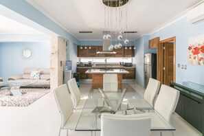 Une cuisine moderne dotée d’un îlot central, de chaises de salle à manger blanches et d’une table à plateau en verre.