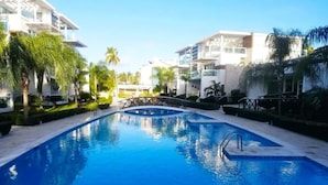 Une piscine à l’eau d’un bleu cristallin, entourée de bâtiments modernes et de palmiers.