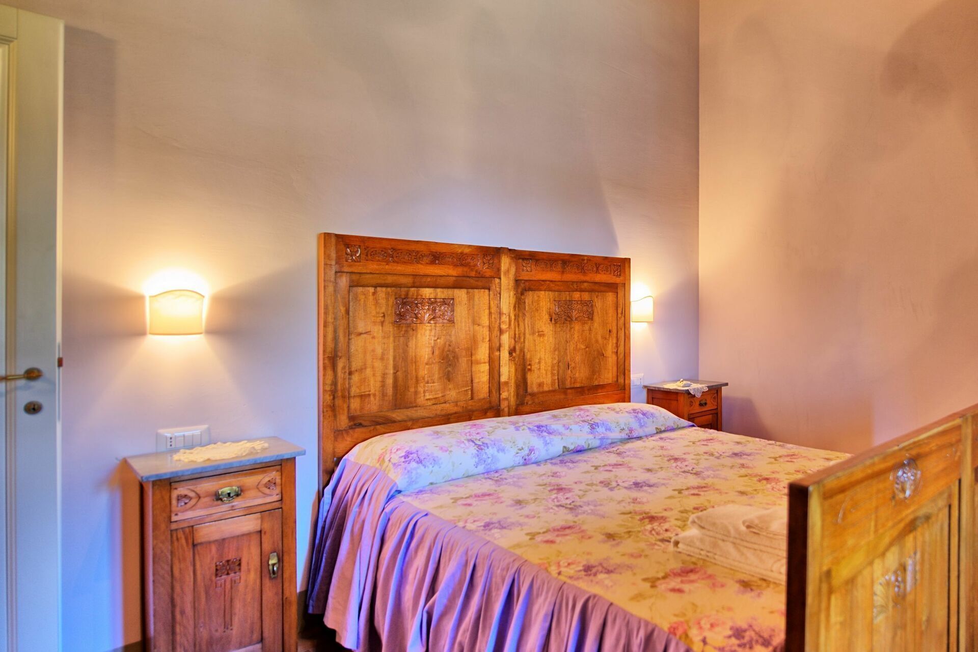 A bedroom with a wooden headboard, a floral bedspread, a nightstand, and a wooden dresser.