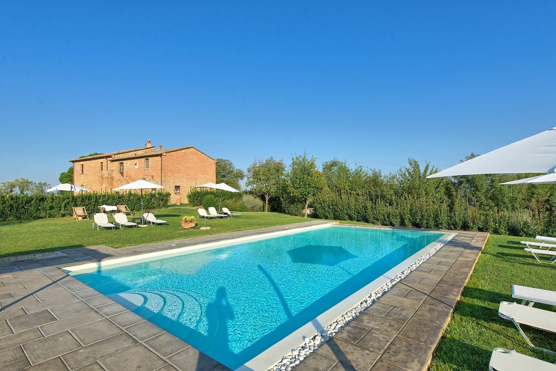 Une piscine rectangulaire, bordée d’une terrasse carrelée, entourée d’une pelouse agrémentée de chaises longues et de parasols.