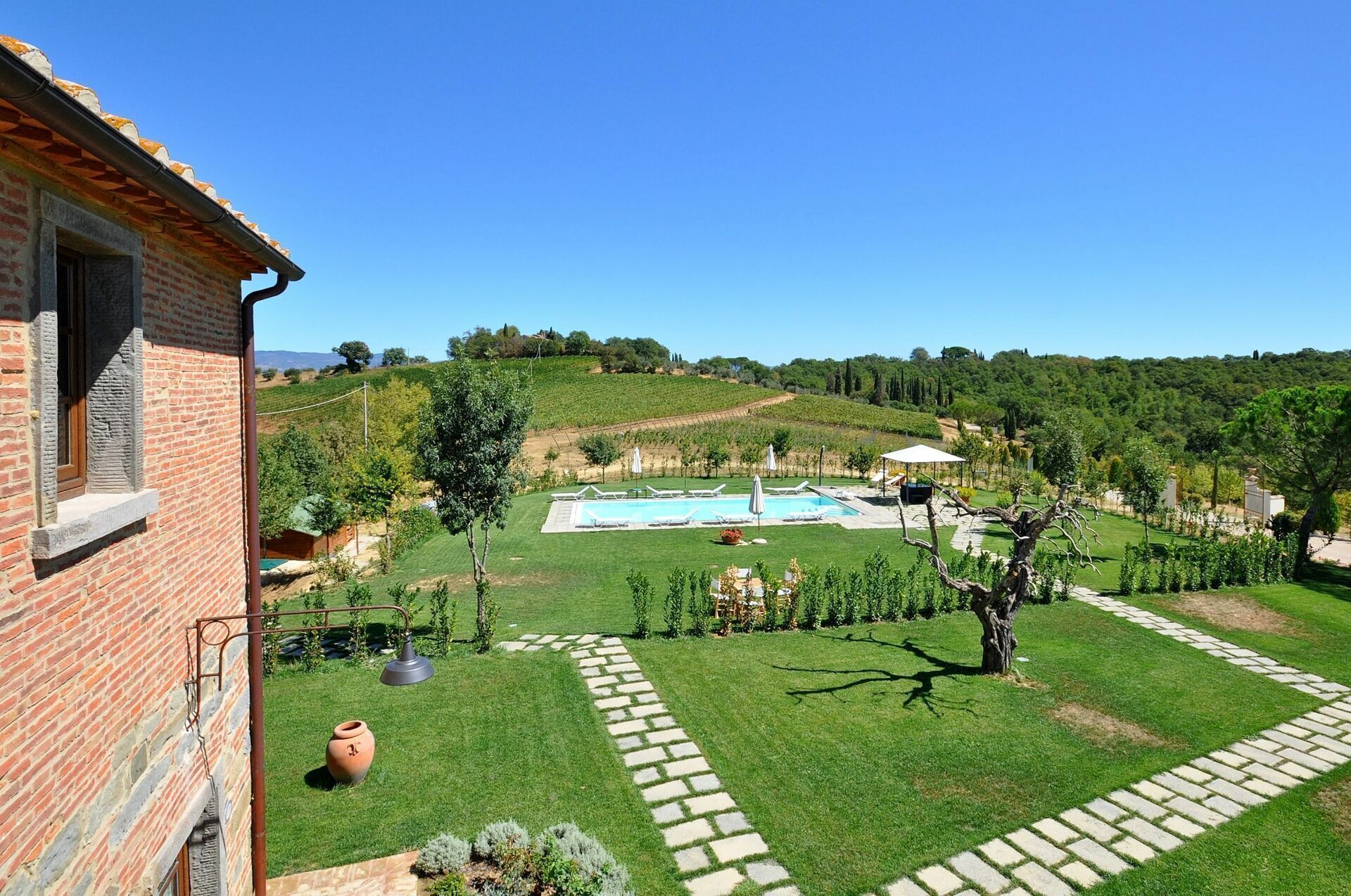 A villa with a swimming pool, a garden, and a vineyard in the background.