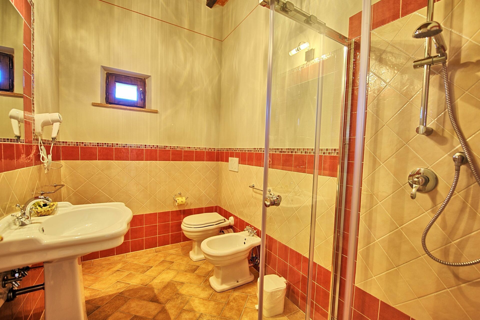 Ein Badezimmer mit Duschkabine, Waschbecken, zwei Toiletten und einem Föhn.