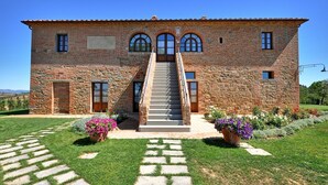 Un edificio de piedra grande con una escalera central, múltiples ventanas y un césped bien cuidado con plantas en macetas.