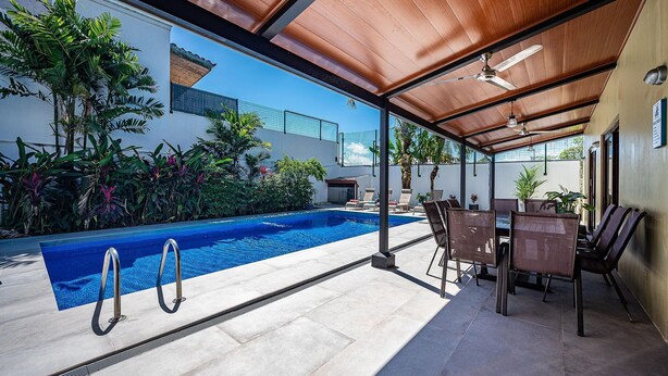 An outdoor swimming pool with a wooden pergola, lounge chairs, and a dining table. - Casa Gris with private pool near the beach in Jaco (Jacó)