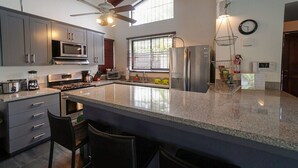 A modern kitchen with granite countertops, stainless steel appliances, and a large island with bar seating. - Casa Gris with private pool near the beach in Jaco (Jacó)